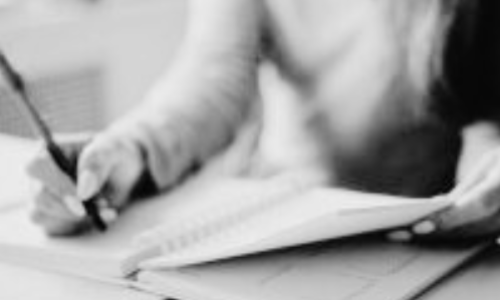 Person writing in a notebook while referencing another document, focusing on work or study.